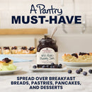 Jar of Stewarts Wild Maine Blueberry Jam on a table with breakfast items, text 'A Pantry MUST-HAVE' and 'Spread over breakfast breads, pastries, pancakes, and desserts'.
