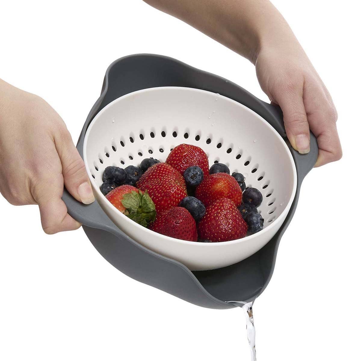 Person holding a colander with strawberries and blueberries over a white background
