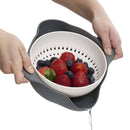 Person holding a colander with strawberries and blueberries over a white background