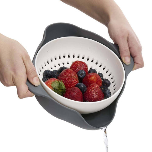 Person holding a colander with strawberries and blueberries over a white background