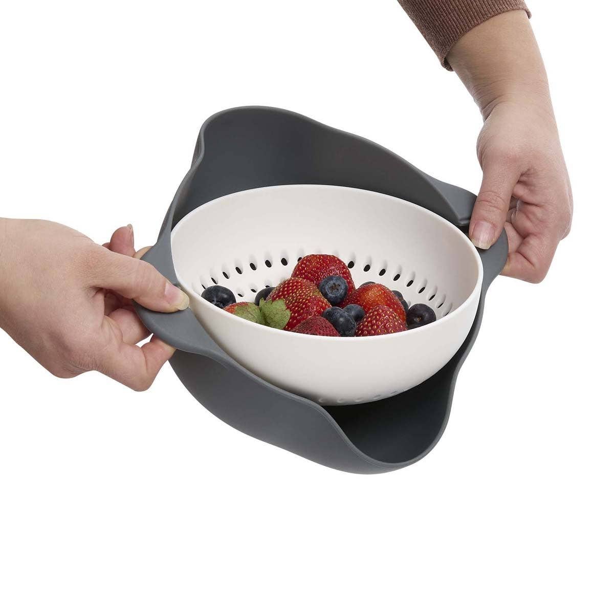 Colander with fruits being held by two hands on a white background