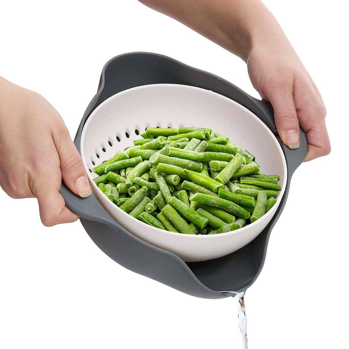 Person holding a colander with green beans against a white background