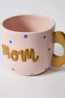 Pink mug with 'mom' in gold letters on a white background