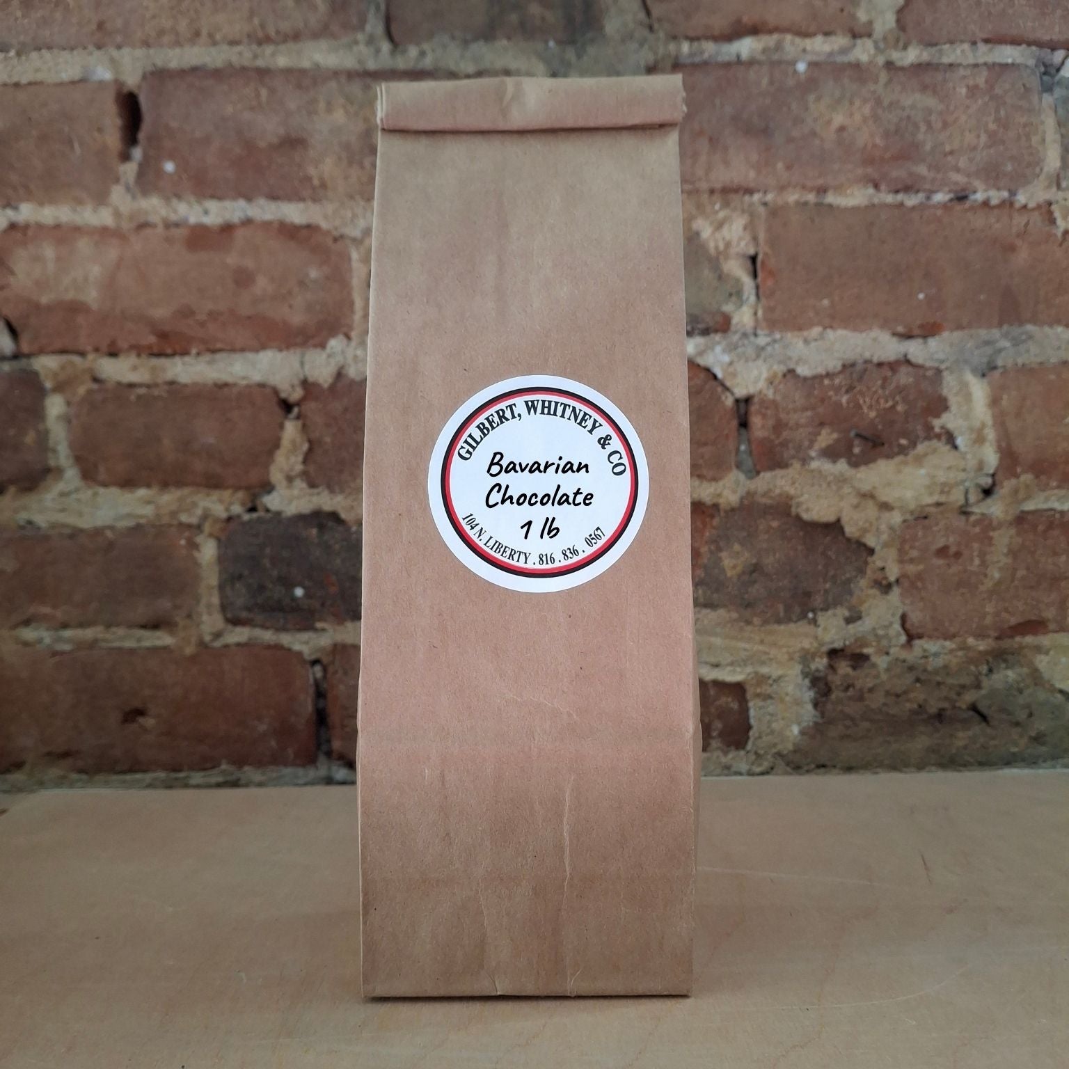 A brown kraft paper bag of coffee standing upright against a rustic brick wall and featuring a round white label reading 'Bavarian Chocolate'