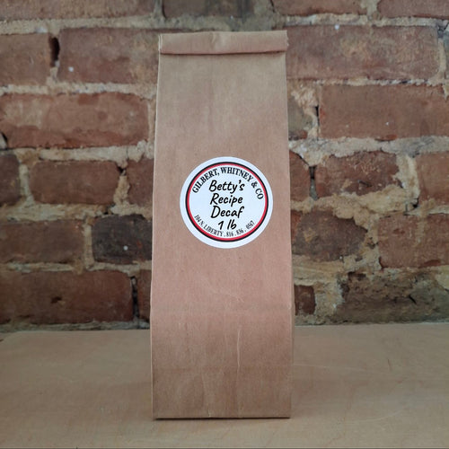 A brown kraft paper bag of coffee standing upright against a rustic brick wall and featuring a round white label reading 'Betty's Recipe'