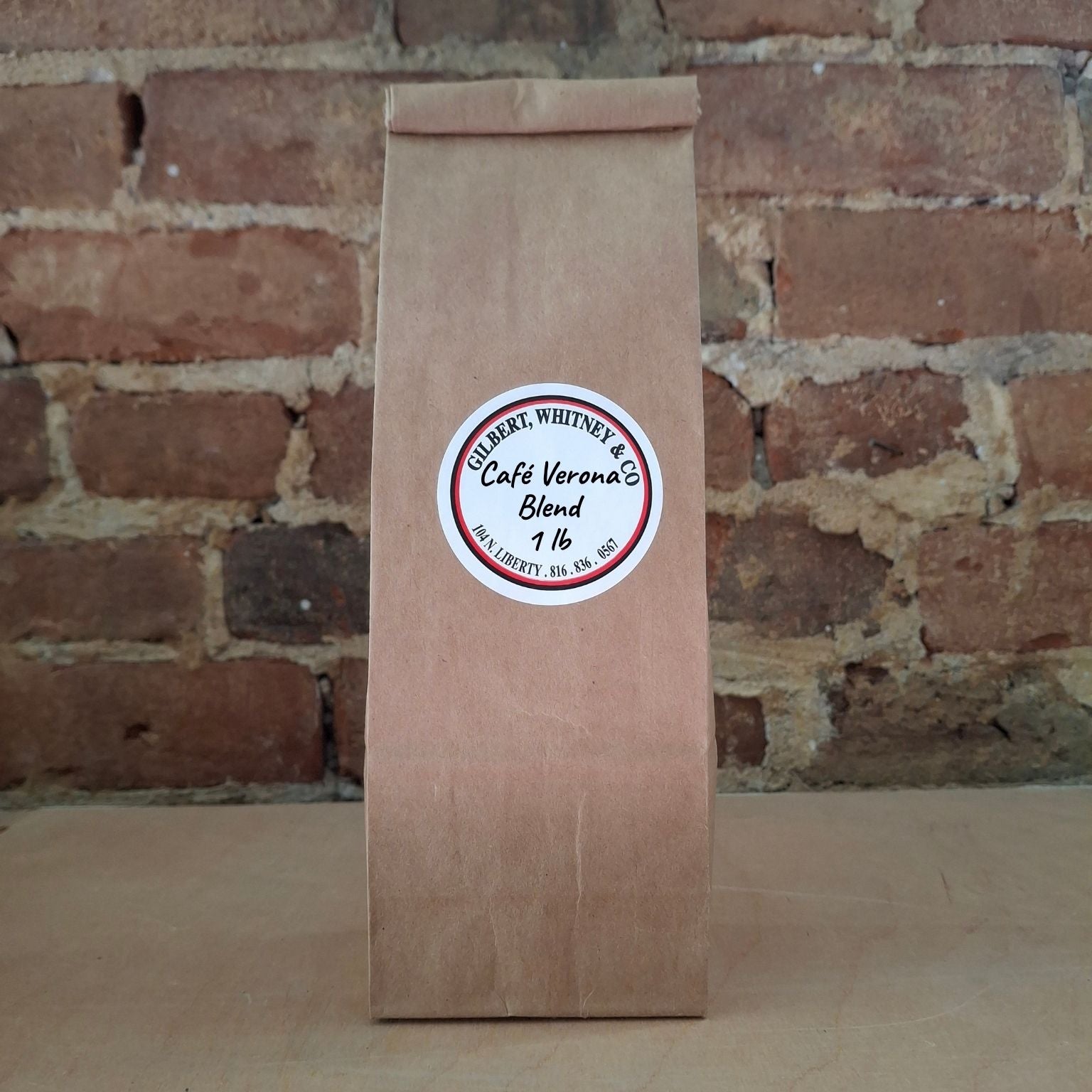 A brown kraft paper bag of coffee standing upright against a rustic brick wall and featuring a round white label reading 'Cafe Verona Blend'