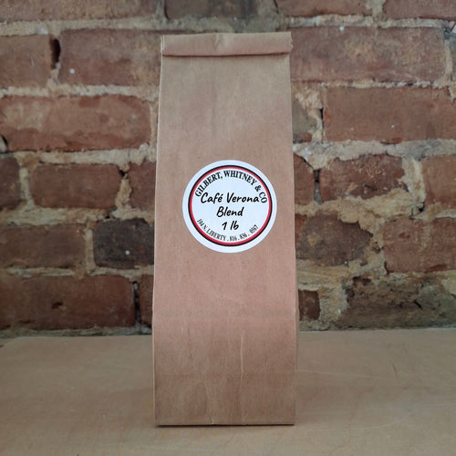 A brown kraft paper bag of coffee standing upright against a rustic brick wall and featuring a round white label reading 'Cafe Verona Blend'