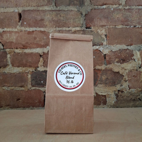 A brown kraft paper bag of coffee standing upright against a rustic brick wall and featuring a round white label reading 'Cafe Verona Blend'