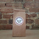 A brown kraft paper bag of coffee standing upright against a rustic brick wall and featuring a round white label reading 'Euro Style Espresso'