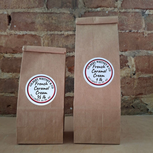 Two brown kraft paper bags of coffee standing upright against a rustic brick wall. Both bags have round white labels reading 'French caramel cream'