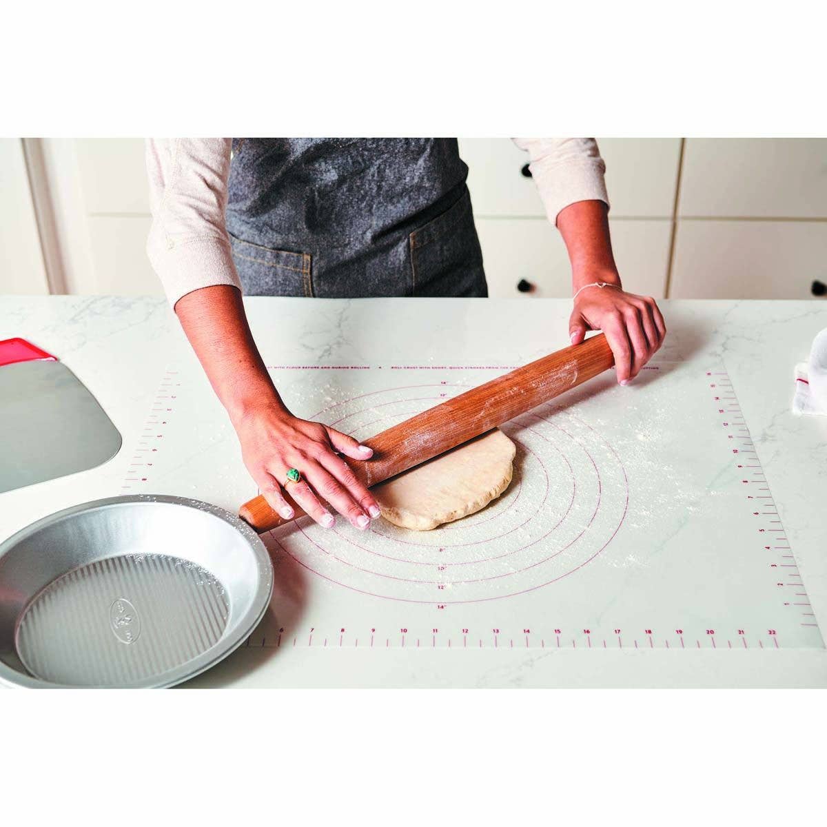 Person rolling dough on a silicone baking mat with a rolling pin.