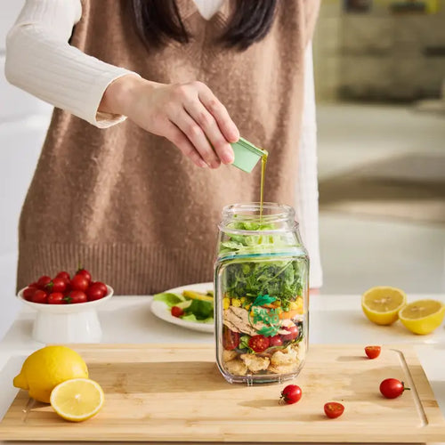 Person preparing a salad in a jar with ingredients on a kitchen counter.