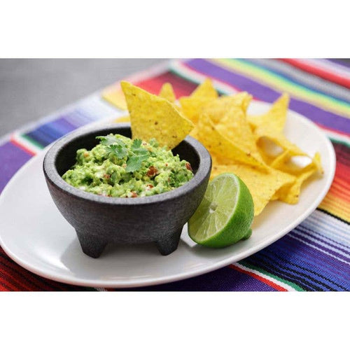 Bowl of guacamole with tortilla chips and a lime on a colorful placemat.