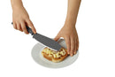 A person's hands holding a large gray serrated kitchen knife over a slice of bread on a white plate, isolated on a white background.