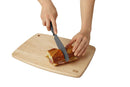 A wooden cutting board with rounded corners on a white background, featuring a person's hands slicing a sandwich with a black-handled knife.