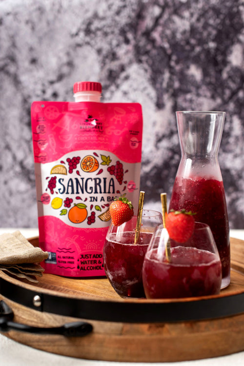 Sangria in a bag with glasses and a carafe on a wooden tray.