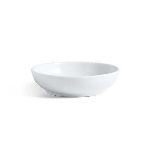 A white porcelain sauce bowl on a green background.