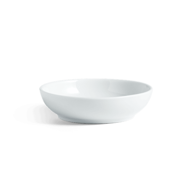 A white porcelain sauce bowl on a green background.