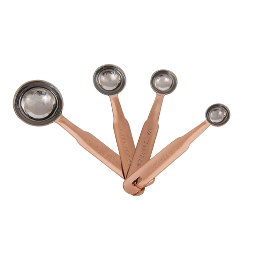 A set of four copper measuring spoons arranged in a fan shape on a plain white background.