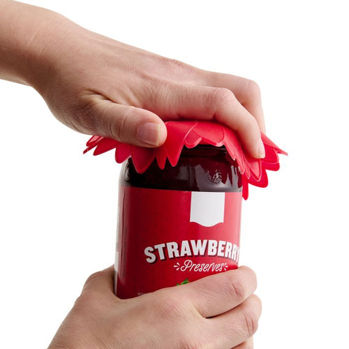 Person using a red flower-shaped jar opener on a strawberry preserve jar.