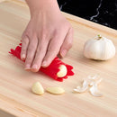 Person using a red silicone jar opener as a garlic peeler on a wooden cutting board with garlic cloves.