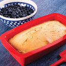 Loaf of bread in a red silicone mold with a bowl of blueberries on a blue surface