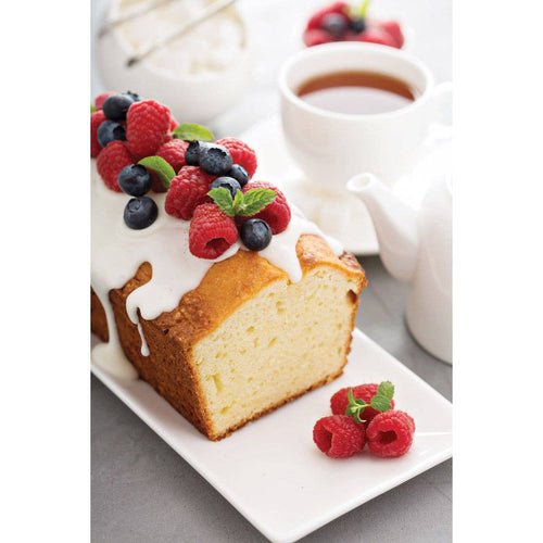 Slice of cake with berries on a plate next to a cup of coffee.