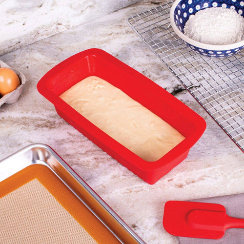 Red silicone loaf pan with unbaked bread dough on a kitchen counter.