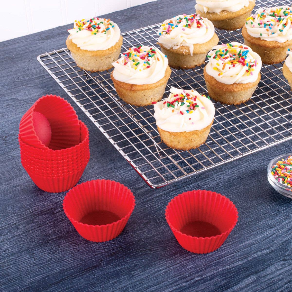 Silicone cupcake liners on a blue surface with cupcakes on a cooling rack.