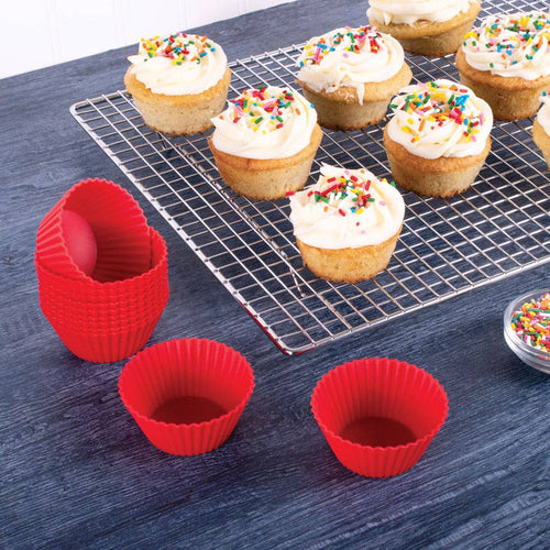 Silicone cupcake liners on a blue surface with cupcakes on a cooling rack.