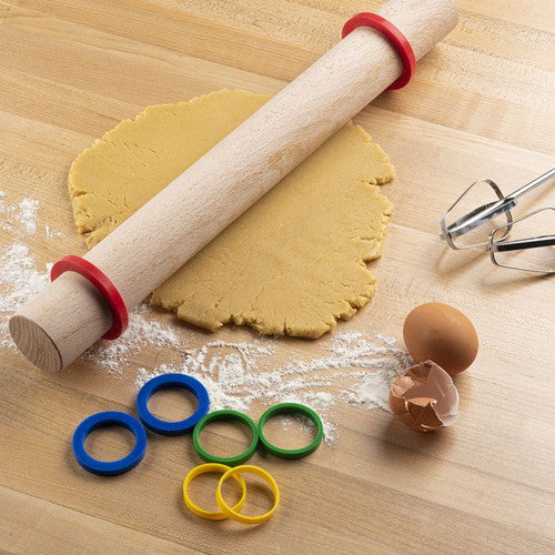 A set of silicone rolling pin rings in various colors placed on a wooden surface with dough and a rolling pin. The rings are designed to fit on the rolling pin to help in rolling out dough evenly.