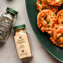 Two bottles of Simply Organic seasonings next to a plate of food on a light surface.