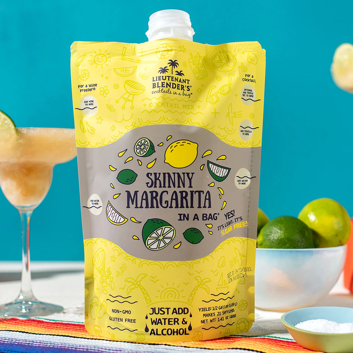 Yellow 'Skinny Margarita in a Bag' package with cocktail ingredients on a colorful tablecloth.