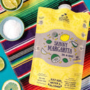 Yellow 'Skinny Margarita in a Bag' package on a colorful striped towel with lime slices and salt.