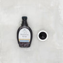 Bottle of blueberry syrup with a small bowl of syrup on a textured white background
