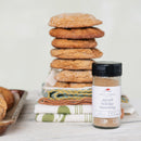 Stack of cookies with a jar of spiced holiday seasoning on a wooden surface.