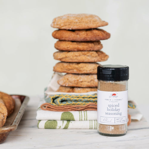 Stack of cookies with a jar of spiced holiday seasoning on a wooden surface.