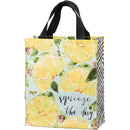 A multicolored tote bag with a pattern of lemons and the text 'squeeze the day' on it, with black and white plaid pattern on the sides and complementing black nylon straps.
