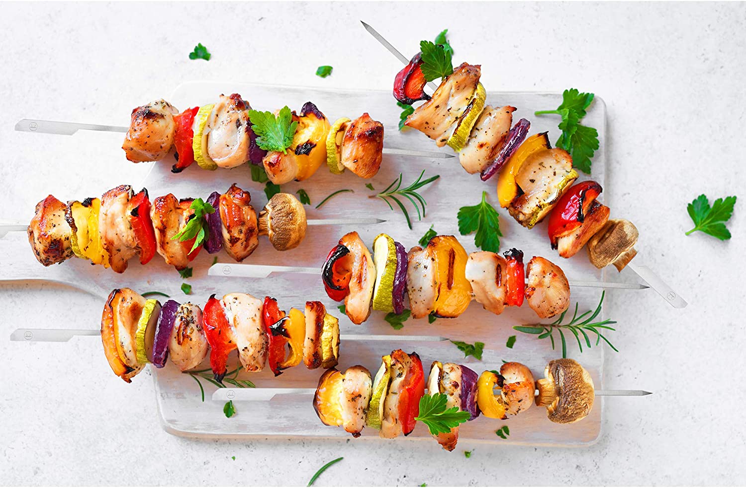Grilled kebabs on a white surface with stainless steel skewers.