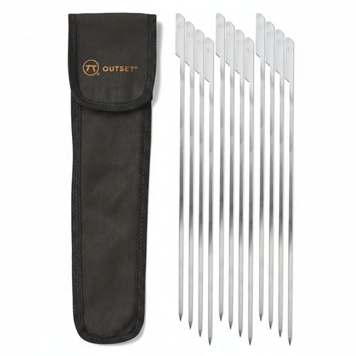 A set of stainless steel paddle skewers with flat handles, accompanied by a dark canvas storage bag with the 'Outset' brand on it.