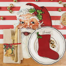 Christmas-themed table setting with Santa Claus face, red stocking table accent on a plate, and gold cutlery on a striped tablecloth.