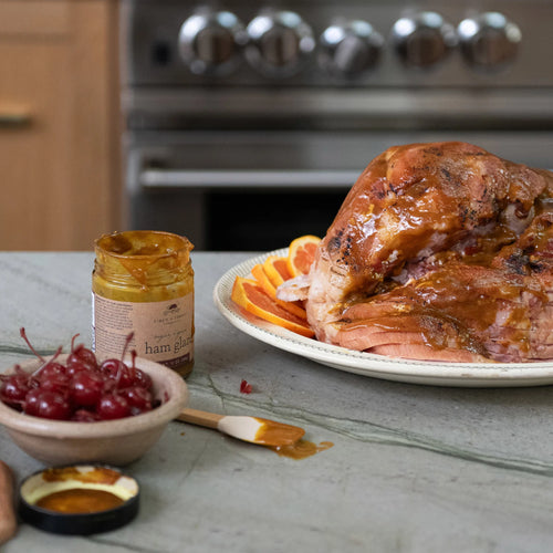 Roasted ham with glaze, cherries, and orange slices on a kitchen counter.