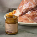 Jar of ham glaze with a ham in the background on a neutral surface