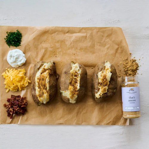 Baked potatoes with various toppings on a brown paper bag with a spice jar labeled 'that's amore' on a white background.
