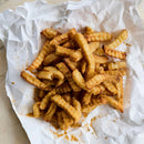Stack of crinkle cut fries with spices on crumpled white paper