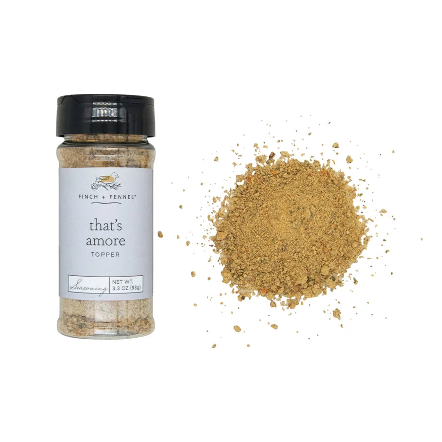 Jar of 'that's amore' topper with a pile of spices beside it on a white background.