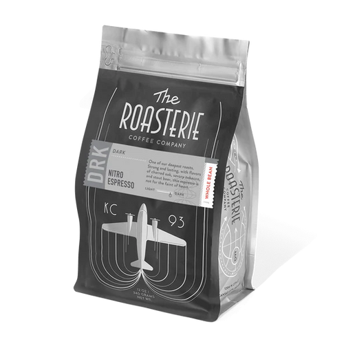 A package of The Roasterie coffee in a clear bag with a black label, featuring a graphic of an airplane and text indicating it is a dark roast nitro espresso.