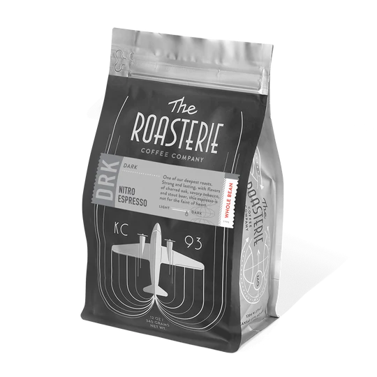 A package of The Roasterie coffee in a clear bag with a black label, featuring a graphic of an airplane and text indicating it is a dark roast nitro espresso.