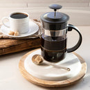 French press filled with coffee on a marble coaster with a cup of coffee and sugar cubes in the background.