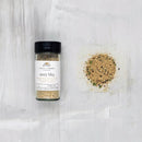 A jar of Finch & Fennel Zesty BBQ seasoning next to a small pile of the seasoning blend spread out on a surface.